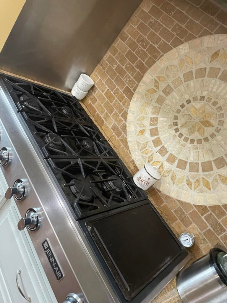 A sparkling clean gas stove top with a decorative tiled backsplash, showcasing a completed kitchen cleaning by Skedaddle Cleaning Services in Eufaula, AL.