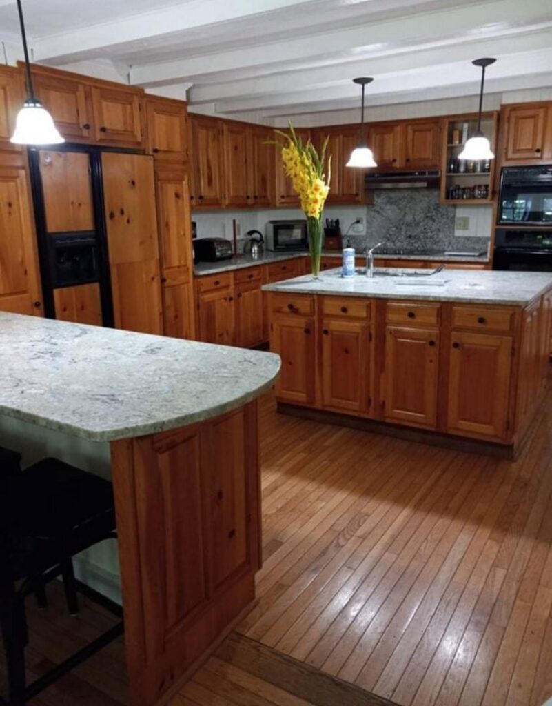 A sparkling clean kitchen with wooden cabinets, granite countertops, and hardwood floors, showcasing Cate's Cleaning Company in Derry, NH.