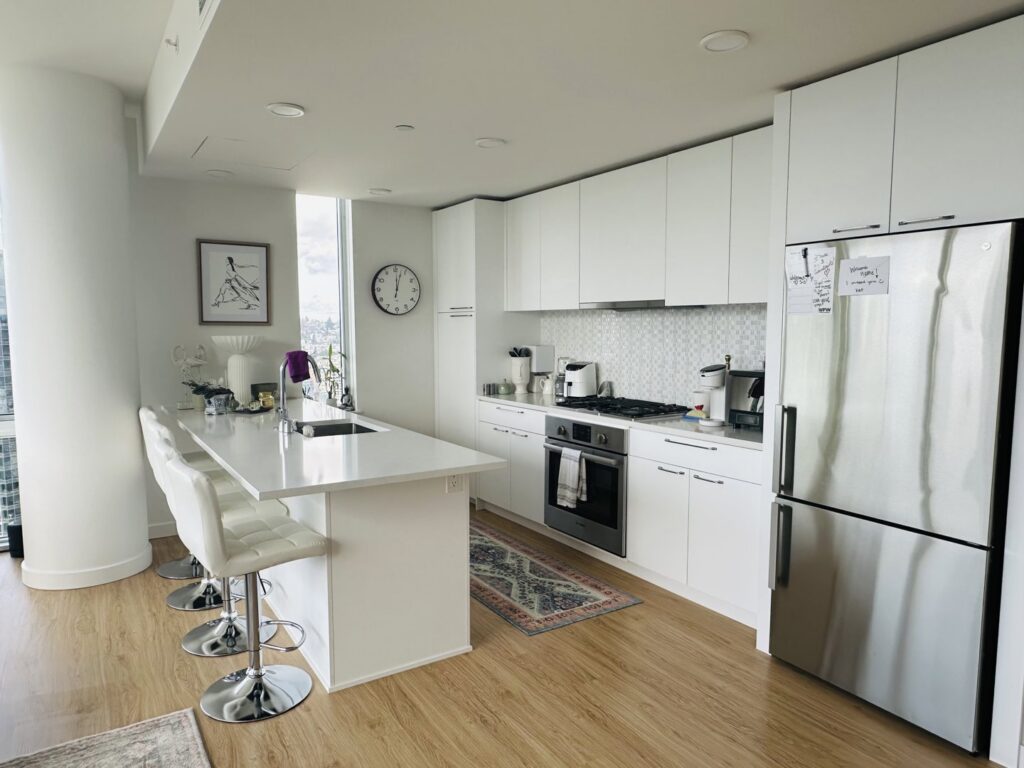 A sparkling clean modern kitchen featuring white cabinets, stainless steel appliances, and a large island, cleaned by Quesada's cleaning services llc in Seattle, WA.