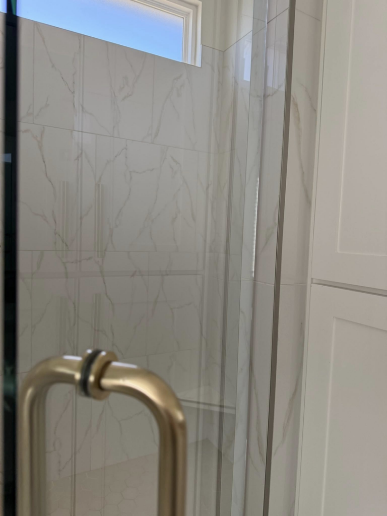 A sparkling clean glass shower door and tiled wall, demonstrating bathroom cleaning services by Global Provisions, AR in Fayetteville, AR.
