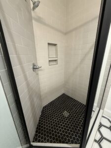 A sparkling clean modern shower with white subway tiles and black hexagonal floor tiles, cleaned by SetApart Home Concierge in Greenville, SC.