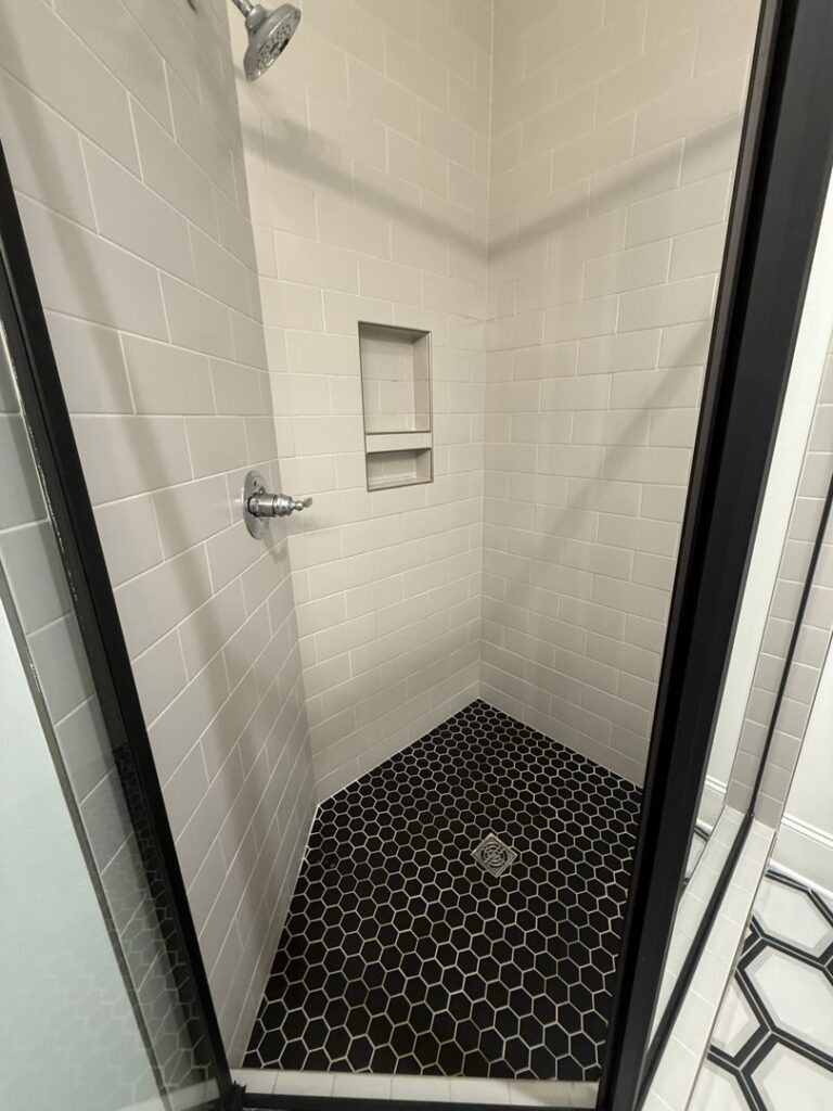 A sparkling clean modern shower with white subway tiles and black hexagonal floor tiles, cleaned by SetApart Home Concierge in Greenville, SC.