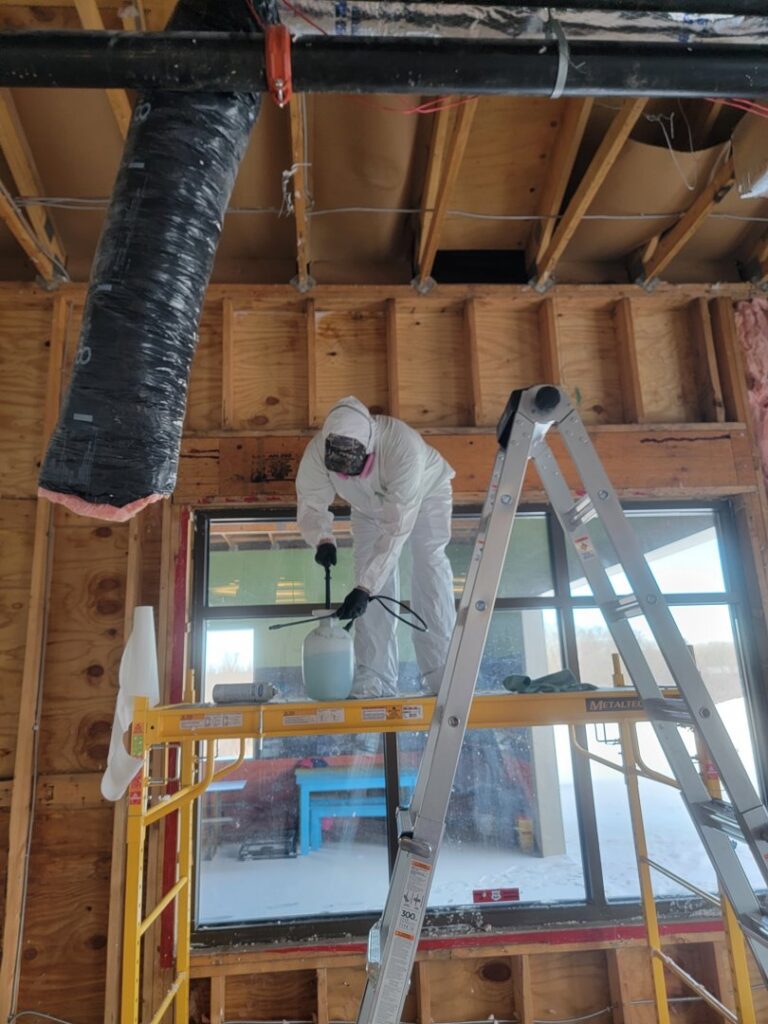 A specialist in a hazmat suit spraying exposed wooden studs during mold remediation by North Shore Restore in Duluth, MN