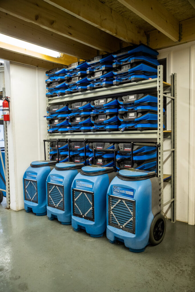A storage rack filled with specialized water damage drying equipment and dehumidifiers at Claim Masters in New Hartford, NY.
