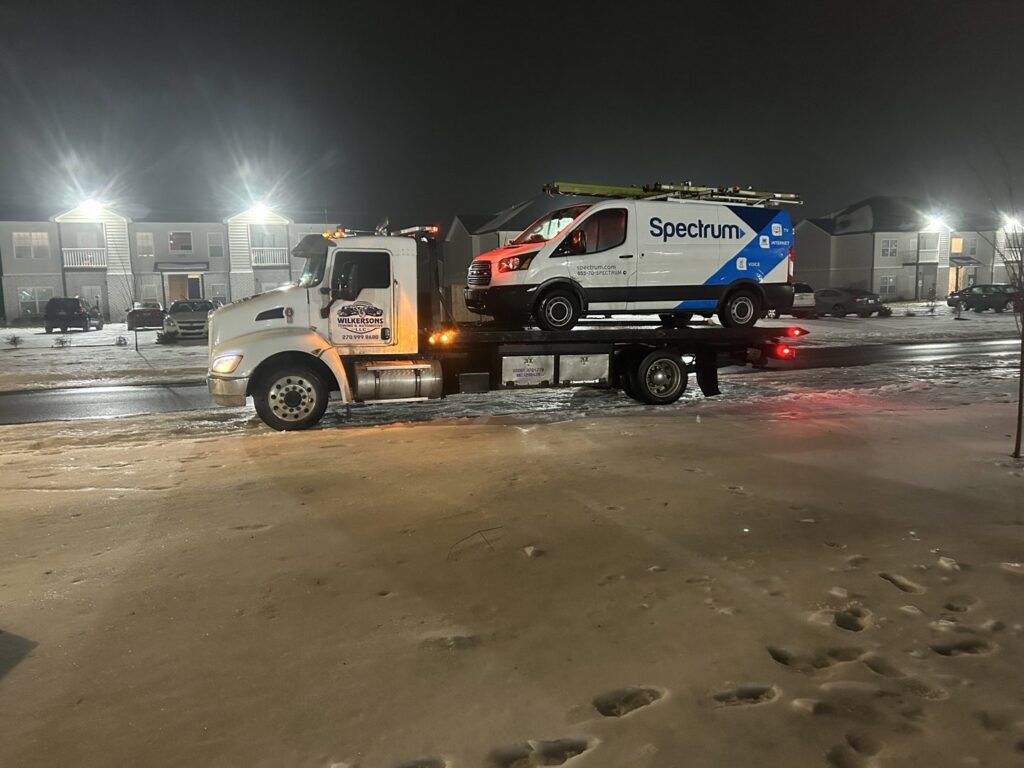 A Spectrum service van loaded onto a flatbed tow truck from Wilkerson's Towing & Automotive LLC at night in Bowling Green, KY.