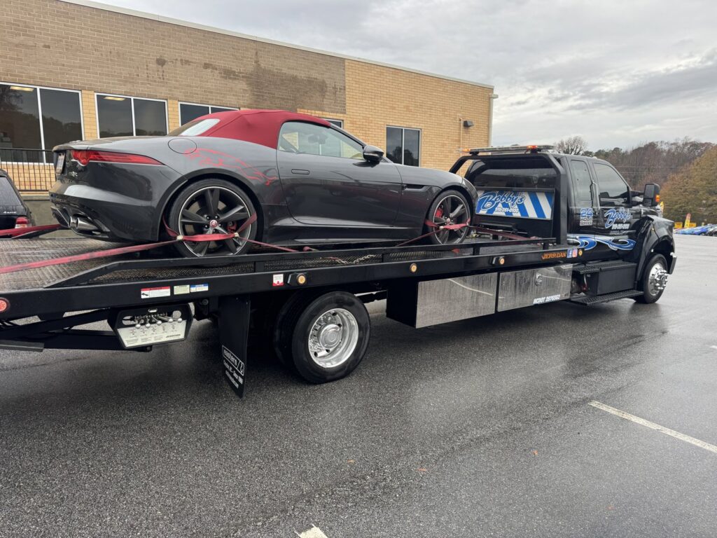 A grey sports car loaded and secured on a Bobbys Towing & Recovery flatbed tow truck in Raleigh, NC.