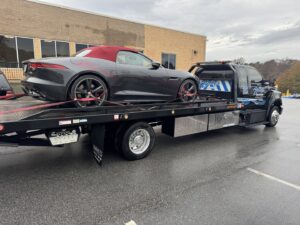 A grey sports car loaded and secured on a Bobbys Towing & Recovery flatbed tow truck in Raleigh, NC.
