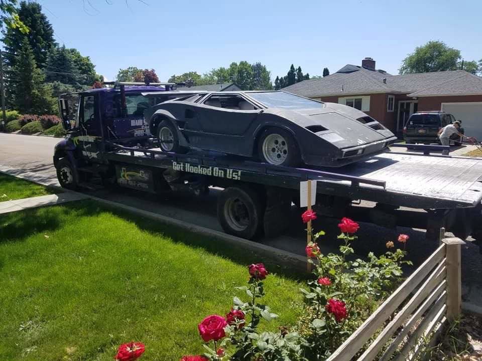 A dark grey sports car being transported on a flatbed tow truck by Idaho State Towing and Recovery in Caldwell, ID.