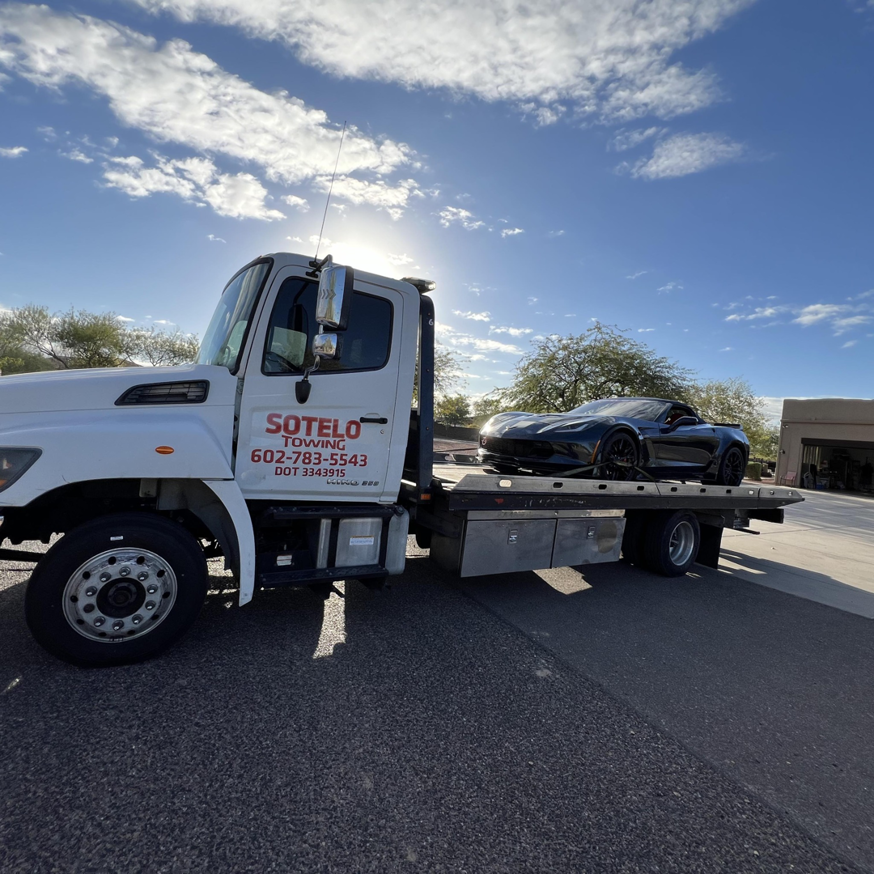 Sotelo Towing LLC providing flatbed towing for a dark sports car under a sunny sky in Phoenix, AZ.