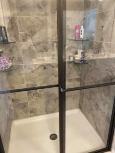 A spotless modern shower with grey tiles and clear glass, professionally cleaned by Tip Top Cleaning in Champaign, IL.