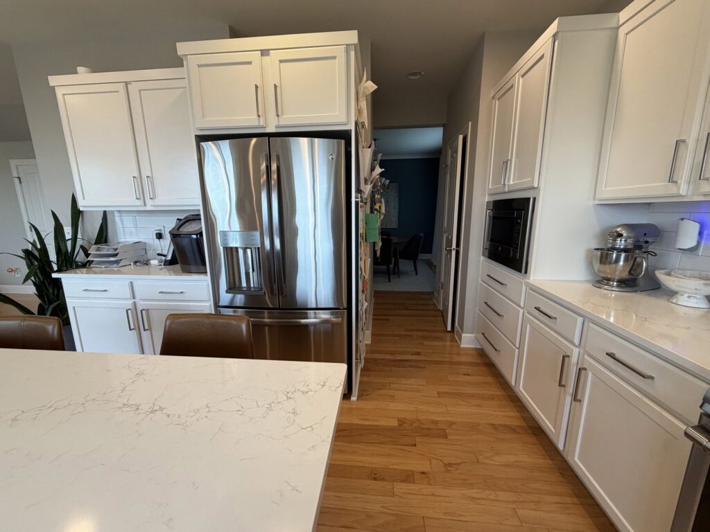 A spotless kitchen with white cabinets, stainless steel appliances, and a large quartz island, expertly cleaned by Quesada's cleaning services llc in Seattle, WA.