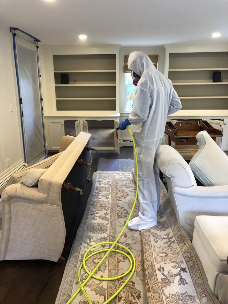 A Green Home Solutions technician spraying a dresser for mold treatment or disinfection after water damage in Mount Airy, MD.