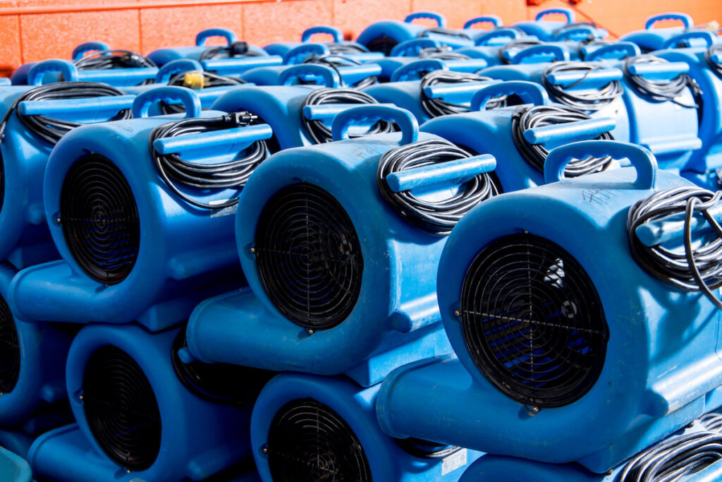 A large stack of blue air movers, essential drying equipment used by Flood Pros for water damage restoration in Sandy, UT.