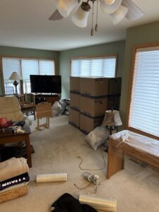 A living room with numerous stacked moving boxes and wrapped furniture, indicating a move by Next Step Moving in Eau Claire, WI.