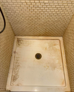 A stained and dirty shower floor before professional cleaning by Carissa's Green Cleaning LLC in Toledo, OH.