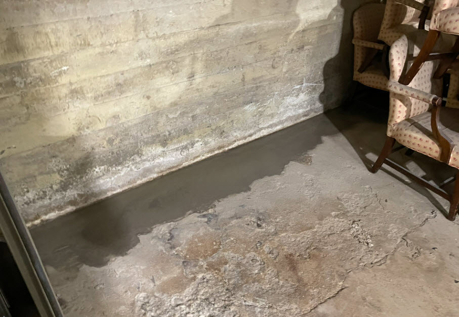 Standing water on a concrete basement floor next to a wall, indicating significant water damage addressed by RestoPros of Salt Lake City, UT