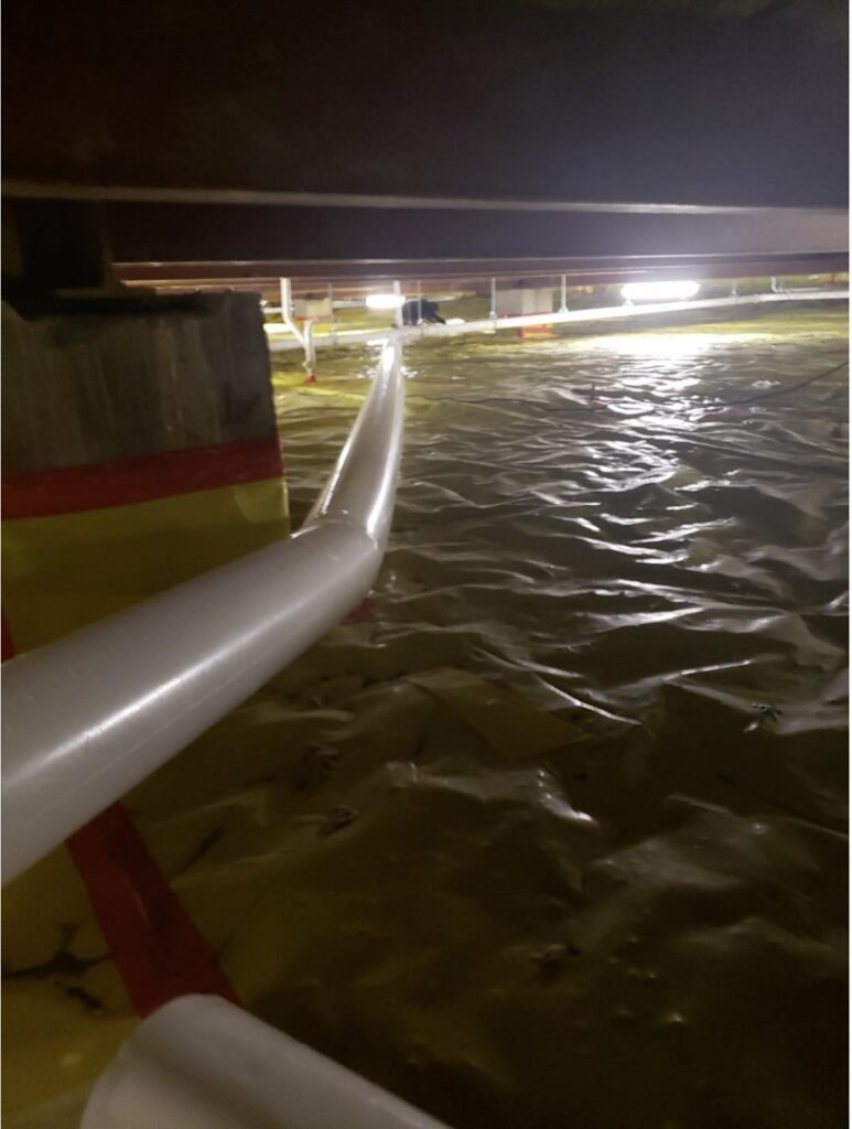 Standing water in a crawl space with a pump hose visible, indicating water extraction by SO-CO Water Damage in Pueblo, CO.