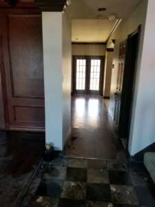 Hallway with dark hardwood floors showing standing water and reflections, indicating water damage, by Dakota Fire and Water Restoration in Bismarck, ND