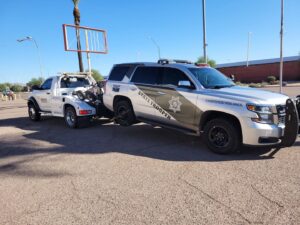 A State Trooper SUV being towed by a wrecker-style tow truck from Caliber Towing in Phoenix, AZ.