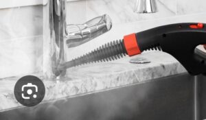 A hand using a steam cleaner attachment to clean a kitchen faucet and sink area by D A E S Cleaning LLC in Billings, MT.