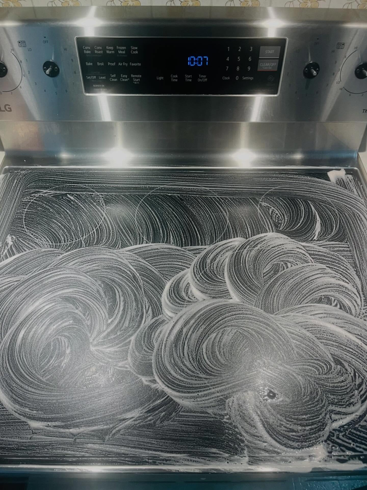 An electric stovetop covered in cleaning solution, actively being scrubbed by BLACK PEARL Cleaning CO. in Greenwood, MO.