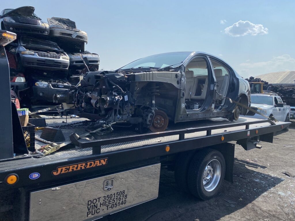 A stripped car chassis being towed on a flatbed truck for junk car removal by Black Mamba Towing & Recovery Llc in Aurora, CO.