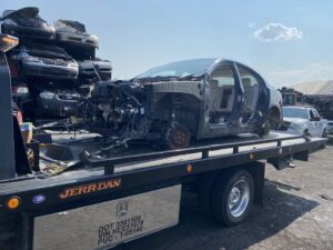 A stripped car chassis being towed on a flatbed truck for junk car removal by Black Mamba Towing & Recovery Llc in Aurora, CO.