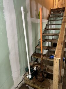 A sump pump and pipes working to remove standing water from a basement, handled by Hull Plumbing, Inc. in Oklahoma City, OK.