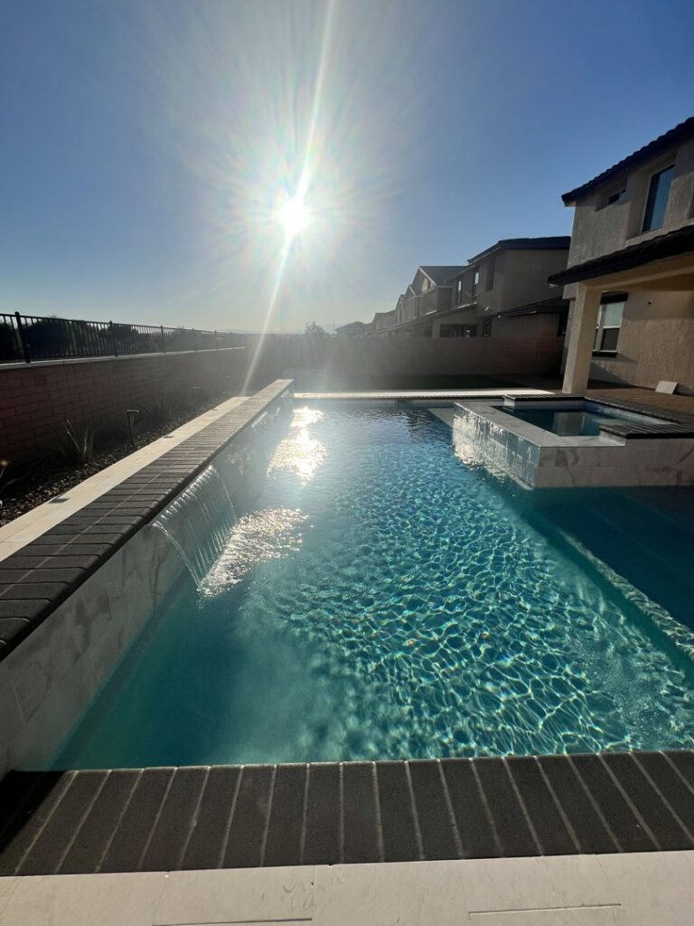 A sunny backyard pool with a spa and elegant waterfalls by Greencare.net POOL Builder in Las Vegas, NV