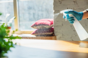 A gloved hand sprays a wooden surface near a window as part of cleaning by Glory Cleaning Service in Irvine, CA.
