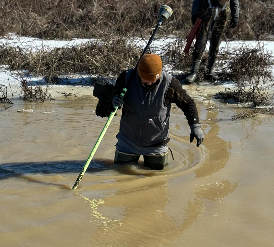 A water damage specialist from Smith & Weiland surveying in muddy water in Clarksdale, MS, wearing waders.