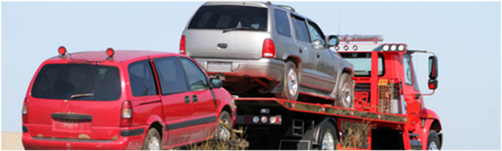 A silver SUV being transported on a red flatbed tow truck by On Time Towing Houston, TX.