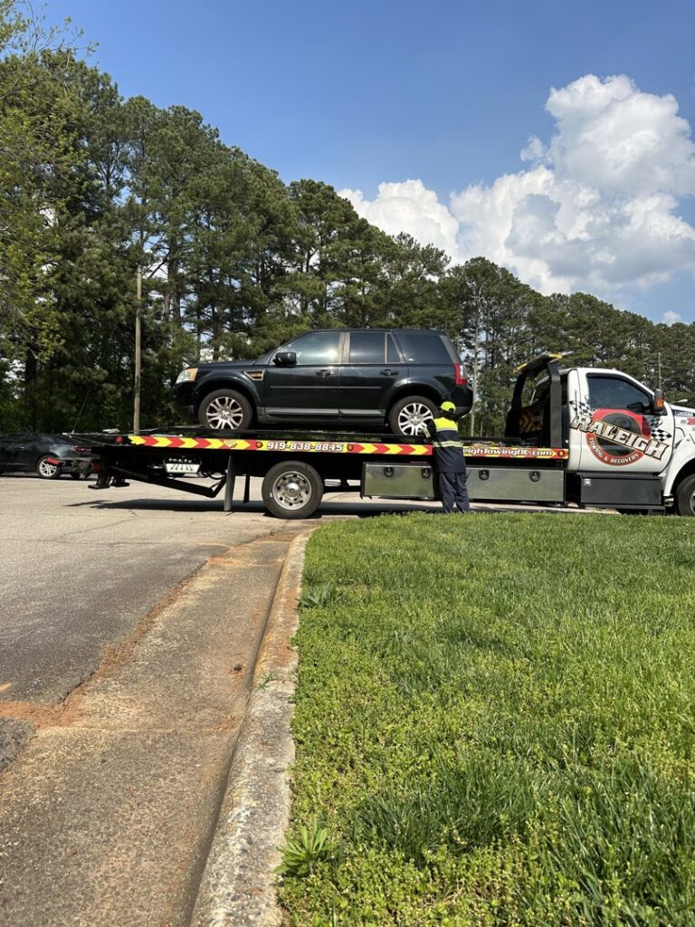 A flatbed tow truck from Raleigh Towing & Recovery loading a black SUV in Raleigh, NC.