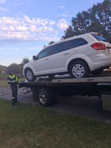 A white SUV being loaded onto a flatbed tow truck by an operator from AMC Towing in Mobile, AL.