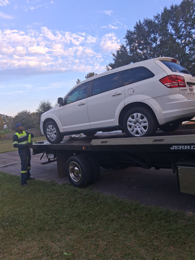 A white SUV being loaded onto a flatbed tow truck by an operator from AMC Towing in Mobile, AL.