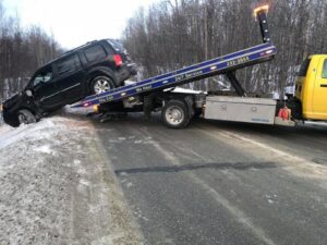 A Help Line Towing truck recovering a black SUV from a snowy ditch on the side of a road in Wasilla, AK.