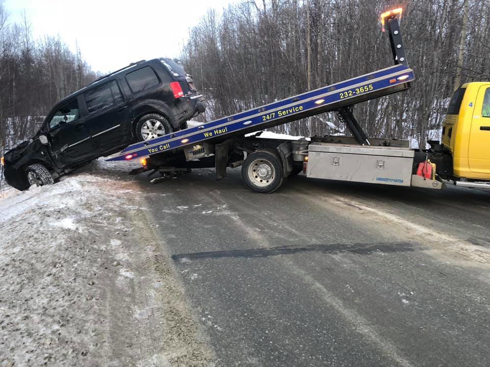 A Help Line Towing truck recovering a black SUV from a snowy ditch on the side of a road in Wasilla, AK.