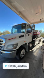 Sotelo Towing LLC transporting a red SUV on a flatbed tow truck at a gas station in Phoenix, AZ.