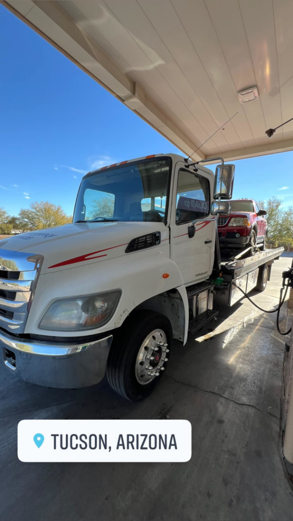 Sotelo Towing LLC transporting a red SUV on a flatbed tow truck at a gas station in Phoenix, AZ.