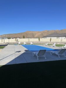 A swimming pool covered with a blue safety cover, surrounded by lounge chairs, indicating pool service by Battle Born Pool & Spa in Sparks, NV.