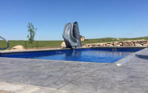 A swimming pool featuring a slide and stamped concrete decking by Backyard Escapes by Kerner Pools & Spas in Bismarck, ND.