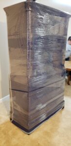 A tall piece of furniture meticulously wrapped in plastic and moving blankets for transport by Emanuel Movers, Inc. in Houston, TX