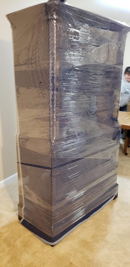 A tall piece of furniture meticulously wrapped in plastic and moving blankets for transport by Emanuel Movers, Inc. in Houston, TX