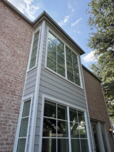 A tall section of a home with new gray siding and large windows installed by Ideal Siding Dallas, TX.