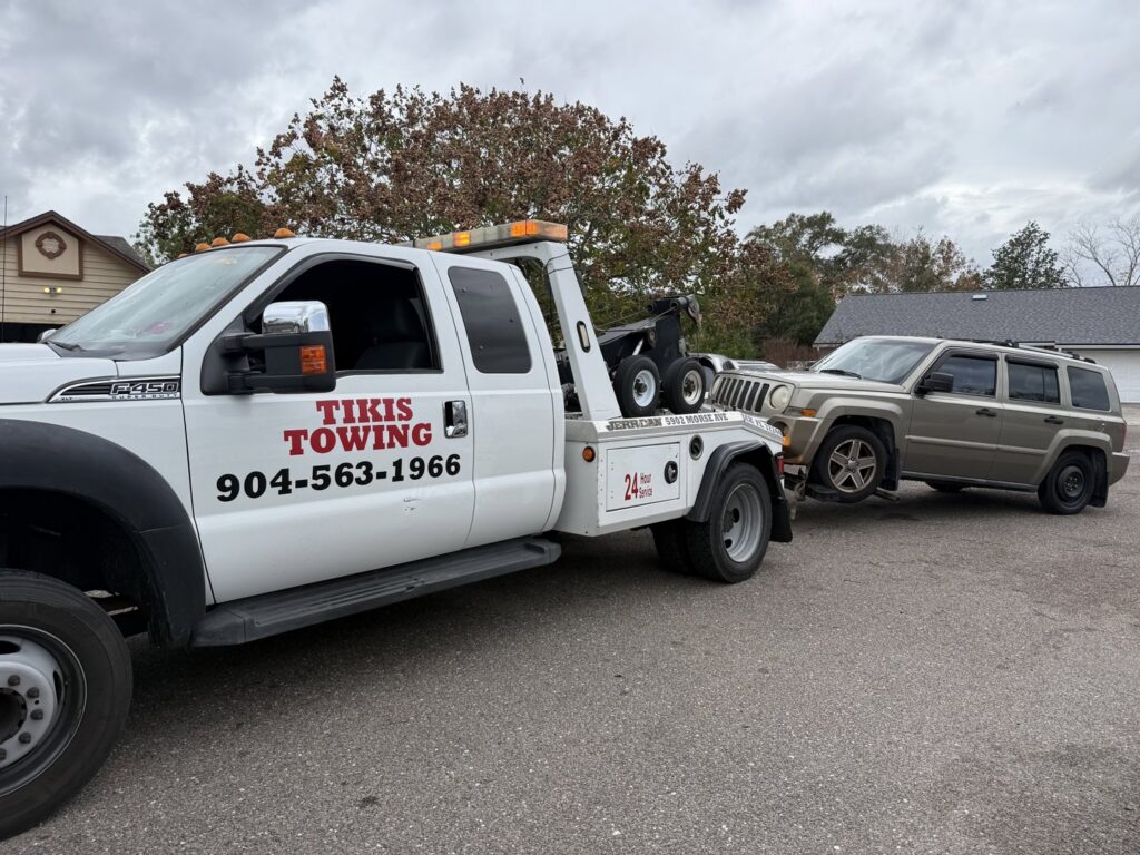 A tan SUV being towed by a wrecker-style tow truck from Tiki's Towing LLC in Jacksonville, FL.