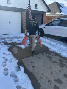 A Paul Davis technician carrying drying equipment through a snowy driveway, ready for a water damage job in Norman, OK.