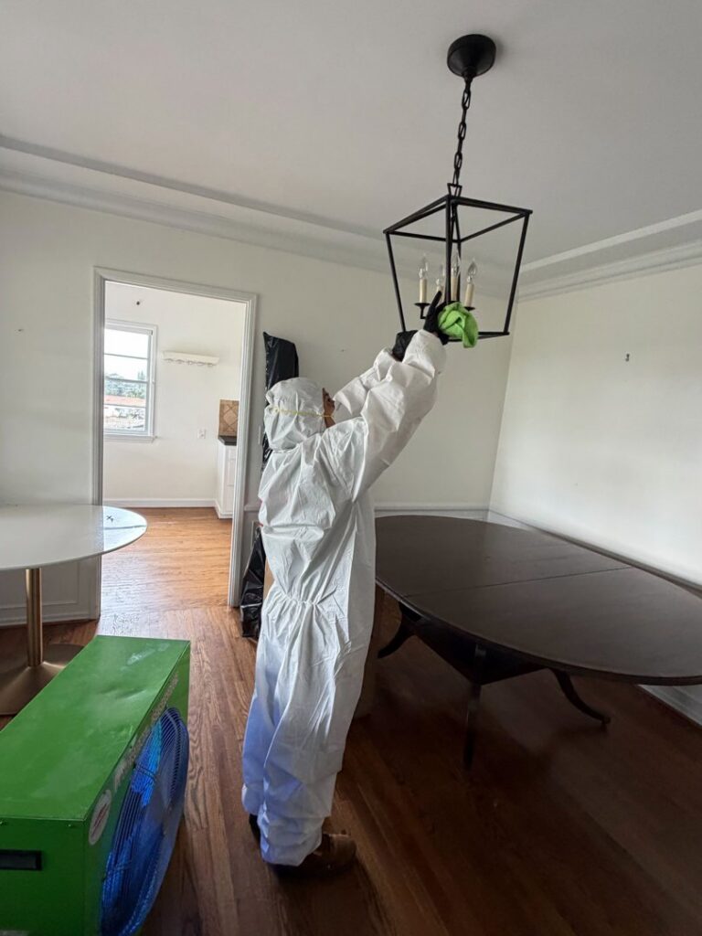 A Servpro of Sandy technician in a protective suit cleaning a chandelier during post-damage restoration in Sandy, UT.
