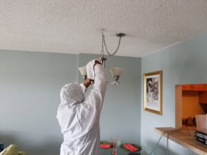 A technician in a protective suit cleaning a chandelier during mold remediation by Southcoast Cleaning Solutions & Restoration in Fall River, MA.