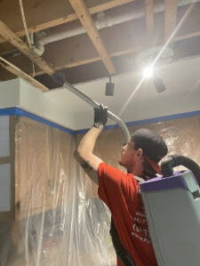 A technician cleaning an exposed ceiling with a specialized tool for remediation by PuroClean of Strafford County in Nottingham, NH.