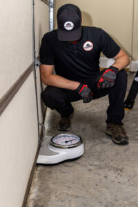 A technician from Access Garage Doors of Treasure Valley diagnosing garage door balance with a scale in Meridian, ID.